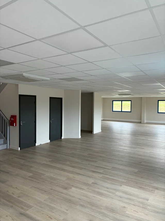 Vue des bureaux avec cloisons blanches, portes grises et sol aspect bois.