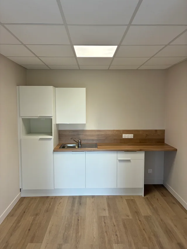 Kitchenette avec meubles blancs, évier et plan de travail aspect bois.